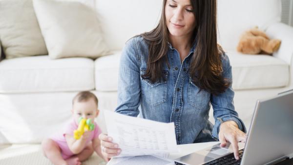 Mother is working with laptop while daughter (6-11 months) is sitting in background
