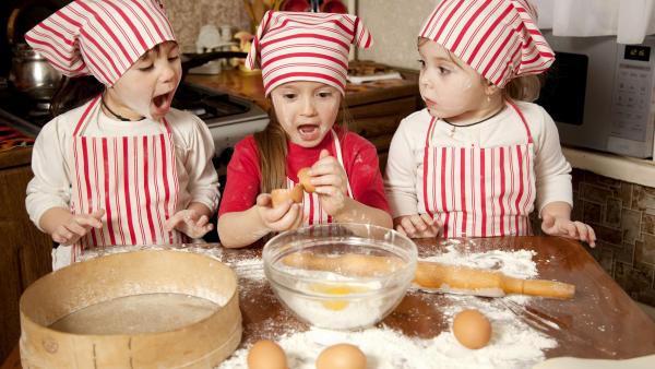 Three little chefs enjoying in the kitchen making big mess. Little girls making bread in the kitchen
