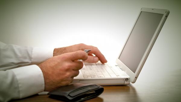 man sitting at desk placing order with credit card on laptop with wallet