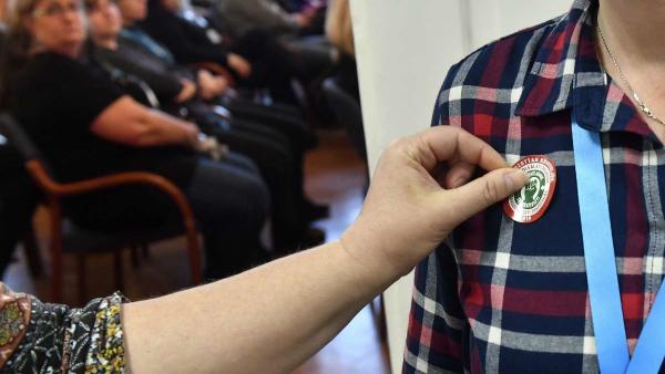 Matricát helyez egy dolgozó munkatársa ruhájára a Magyar Köztisztviselõk, Közalkalmazottak és Közszolgálati Dolgozók Szakszervezete (MKKSZ) egynapos sztrájkjának elindításán tartott gyûlésen a XV. kerületi polgármesteri hivatalban 2019. március 14-én.
MTI